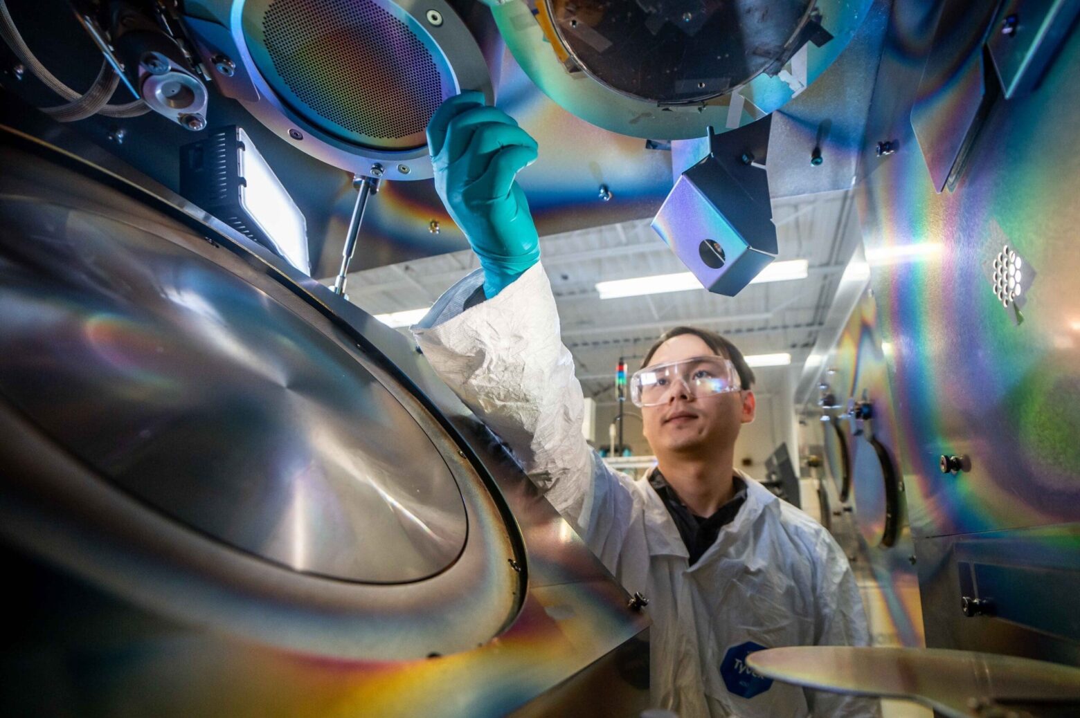 alt = Scientist working inside a Angstrom Engineering reticle system (thin-film deposition system), adjusting components of a vacuum chamber used for semiconductor, OLED, and materials research.