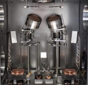 alt = Inside of a sputtering and electron beam (e-beam) deposition chamber. The chamber has two angled e-beam sources, precision mounts, and other mechanical components.