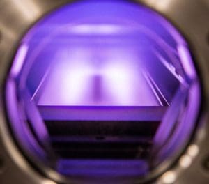 alt = close up view of a High-Power Impulse Magnetron Sputter system. It is illuminated with a purple light, highlighting the target and surfaces. It demonstrates the technologically advanced systems that Angstrom Engineering creates.