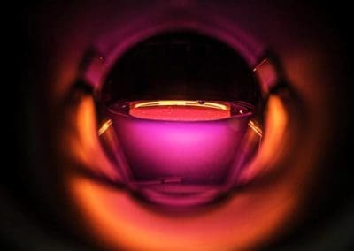 alt = Interior of an RF (Radio Frequency) bias stage. A circular platform illuminated by orange and purple light. It is used to add a controlled bias to a substrate.