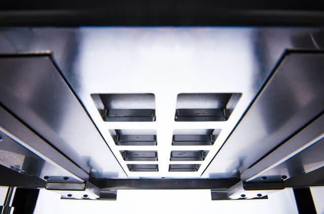 alt = Close-up of a heated stage. The central area is glowing with an orange light, indicating high temperatures. The surroundings are dark, contrasting with the bright heated section in the middle. It is enclosed, with visible metal parts that guide the heat.
