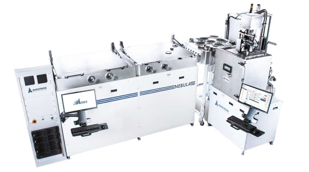 LinearSputter alt = A linear sputter system made by Angstrom Engineering, from the 'NEBULA’ series. The system has a series of interconnected white units with multiple chambers and control panels. Two digital monitors with keyboard interfaces display the AERES software with operational data. The setup highlights how much work is needed for design of deposition machines and what Angstrom Engineering equipment looks like.